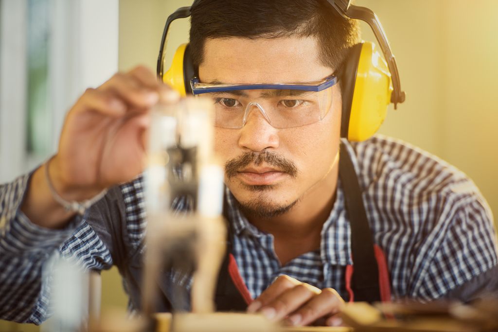 Carpenter wearing protection gear measuring wood in a workshop with great focus and precision.