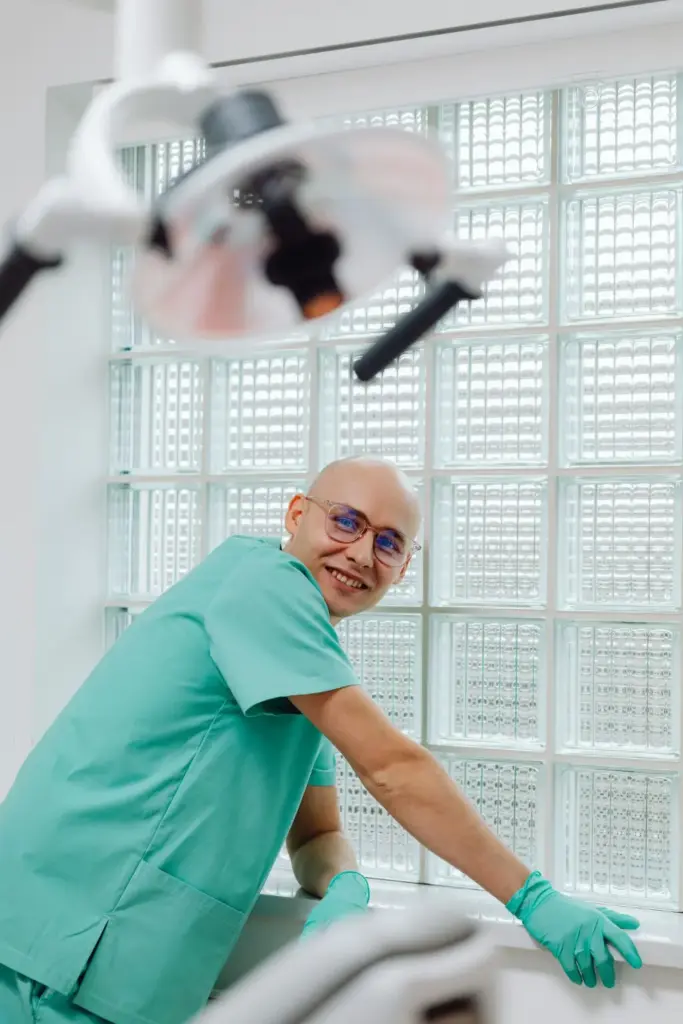 A cheerful dentist in teal scrubs in a modern clinic, ready for patient care.